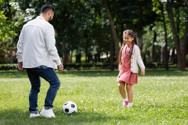 Smiling asian child playing football with father in summer park 