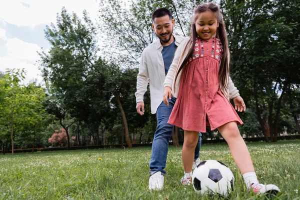 Low angle view of smiling asian family playing soccer in summer park 