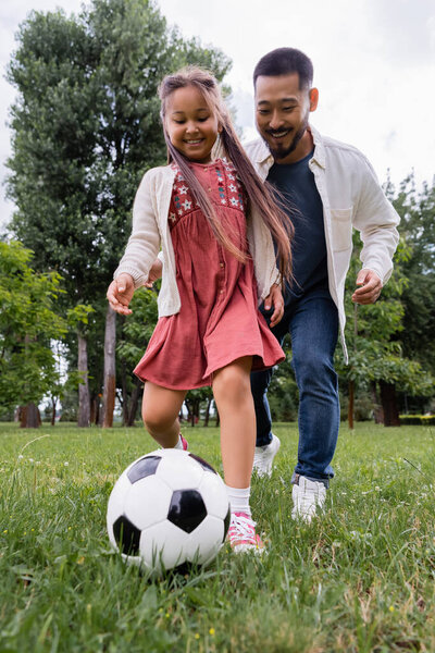 Wide angle view of cheerful preteen girl playing soccer with father in park 