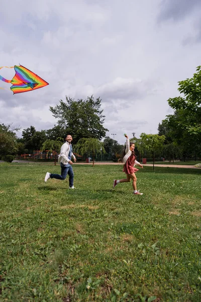 Positive Asian Man Running Daughter Flying Kite Park — Fotografia de Stock