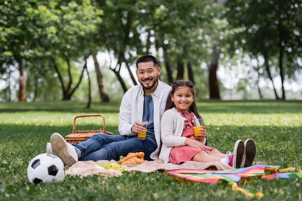 Smiling Asian Family Holding Orange Juice Food Football Blanket Park —  Fotos de Stock