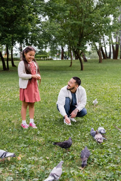 Asian parent and daughter feeding birds in summer park