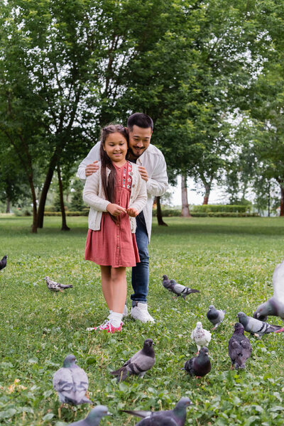 Asian parent hugging daughter near birds in summer park 
