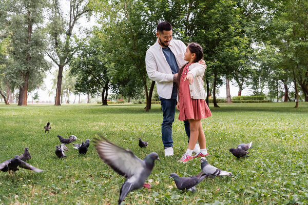 Asian kid pointing at doves near father in summer park 