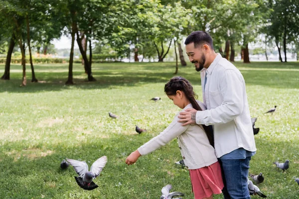 Asian dad hugging daughter near birds in summer park 