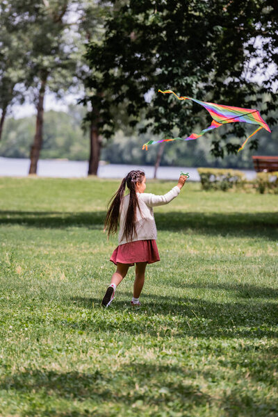 Asian girl playing with colorful flying kite in summer park 