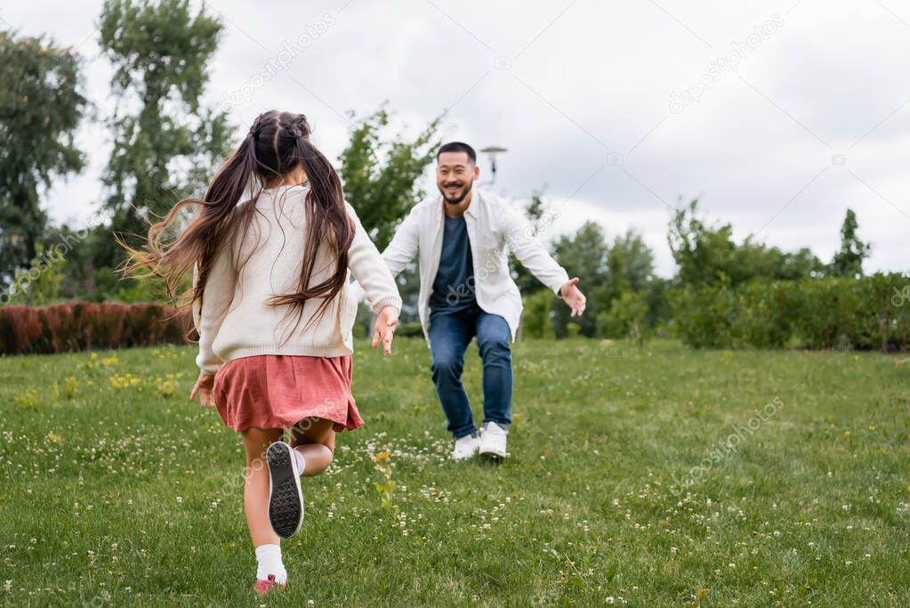 Preteen girl running to asian dad in summer park 
