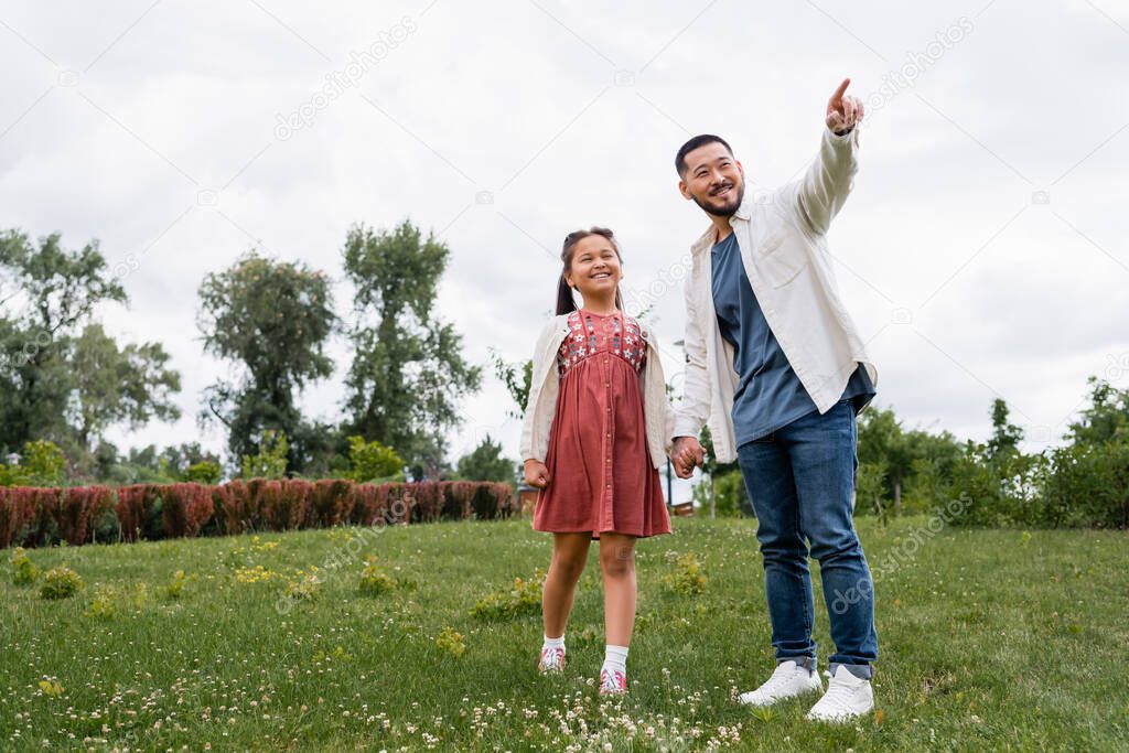 Cheerful asian daughter and dad looking away in summer park 