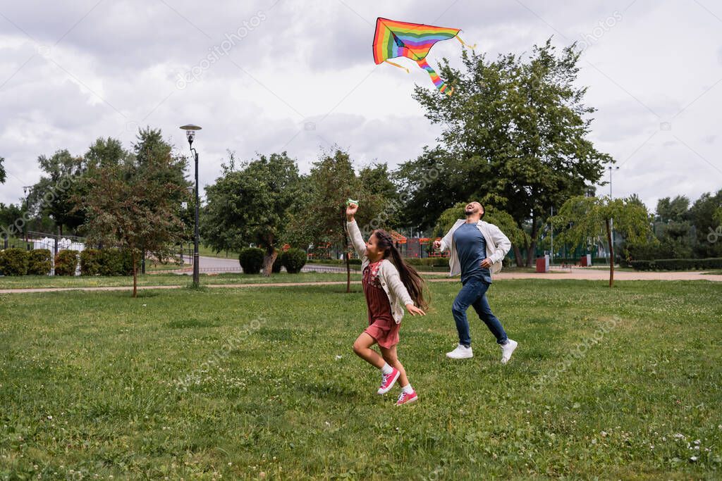 Happy asian family playing with flying kite in summer park 