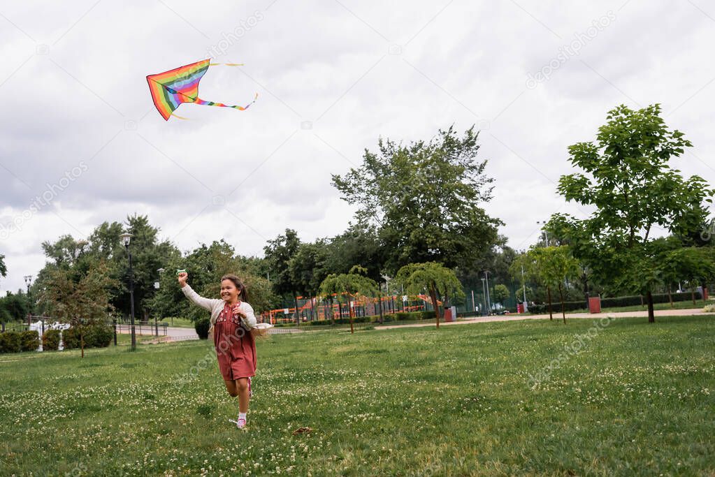 Happy asian girl holding flying kite while running in park 