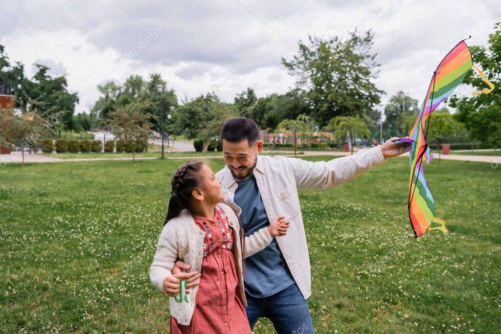 Smiling asian parent holding flying kite near child in park 