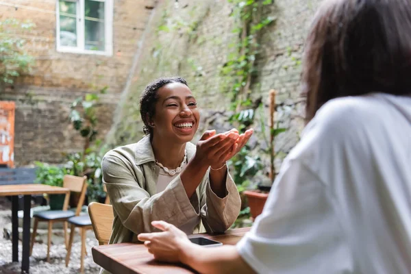 Веселая Африканская Американка Разговаривает Другом Возле Смартфона Кафе Открытом Воздухе — стоковое фото
