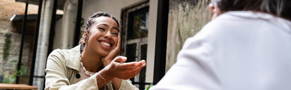 African american woman smiling while talking to friend in outdoor cafe, banner 