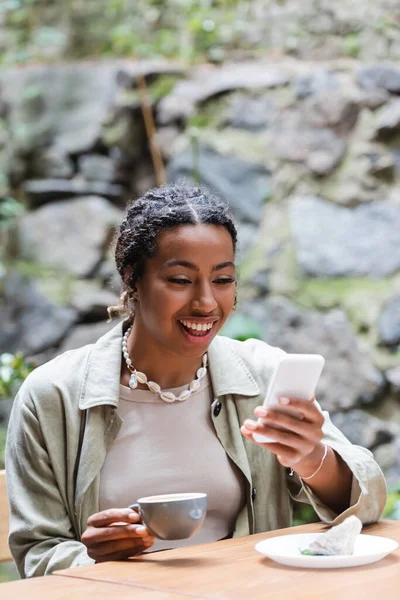 Cheerful African American Woman Using Smartphone Holding Coffee Dessert Terrace —  Fotos de Stock