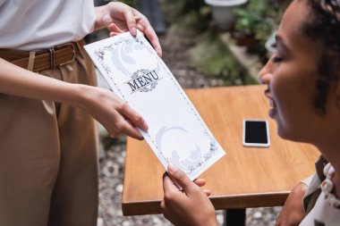 Blurred african american woman taking menu from waitress on terrace of cafe 