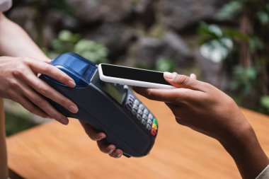 Cropped view of african american woman paying with smartphone near waitress in outdoor cafe 
