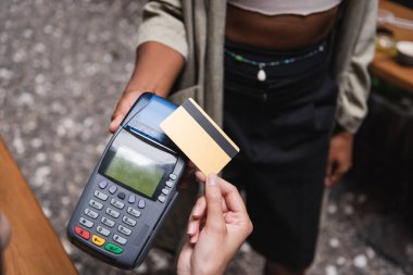 Cropped view of client paying with credit card near african american waitress in outdoor cafe 