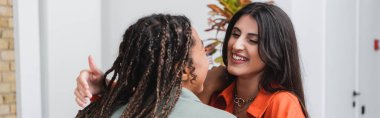 Smiling woman hugging african american girlfriend in cafe, banner 