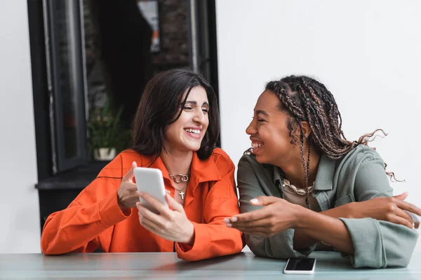 Laughing Interracial Girlfriends Using Mobile Phone Cafe — Stockfoto