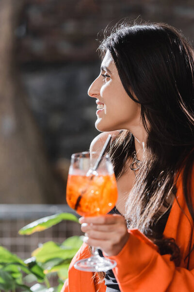 Side view of smiling woman holding blurred cocktail in cafe 