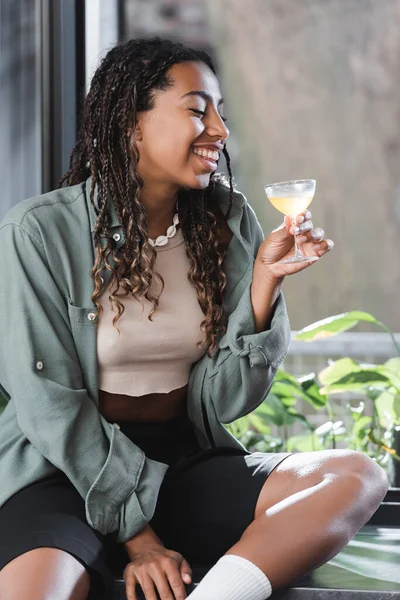 Smiling African American Woman Holding Cocktail While Sitting Windowsill Cafe — Stock Fotó