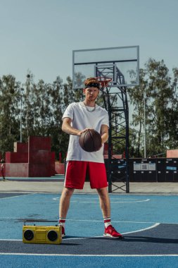 full length of sportive man holding ball while standing on court near boombox