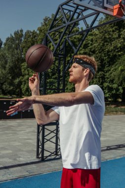 young basketball player in white t-shirt spinning ball on finger outdoors