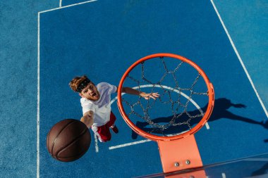 top view of young excited man throwing ball into basketball ring