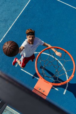 top view of redhead excited man throwing ball into basketball hoop clipart