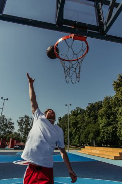 man in white t-shirt throwing ball into basketball hoop on court