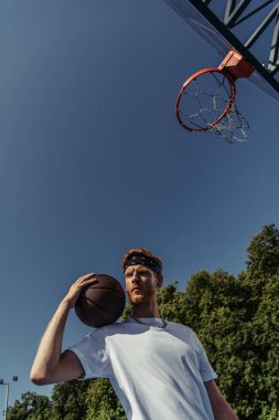 low angle view of sportive man standing with ball under basketball hoop