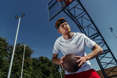 low angle view of man in bandana and white t-shirt playing basketball outdoors