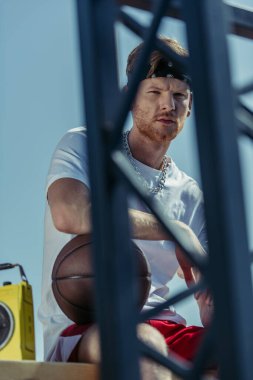 sportsman with ball looking at camera through blurred fence on stadium
