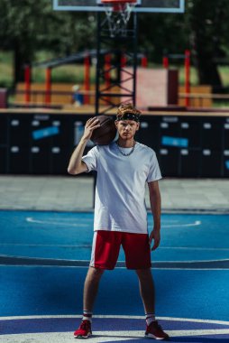 full length of basketball player in red shorts and sneakers looking at camera on modern court