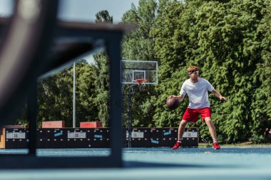 full length of man in sportswear playing basketball outdoors on blurred foreground