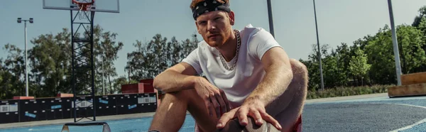 basketball player in bandana sitting on court and looking at camera, banner
