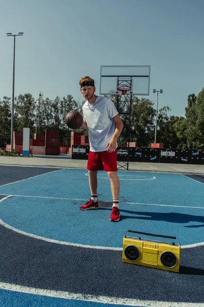 full length of basketball player standing on court near boombox