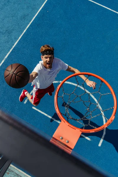 top view of redhead excited man throwing ball into basketball hoop