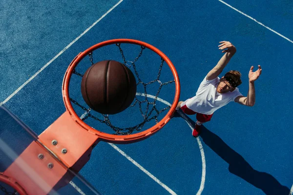 top view of ball in basketball ring and young man training on court