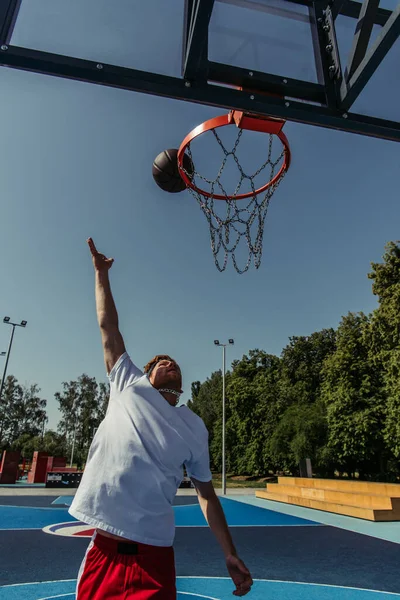 man in white t-shirt throwing ball into basketball hoop on court