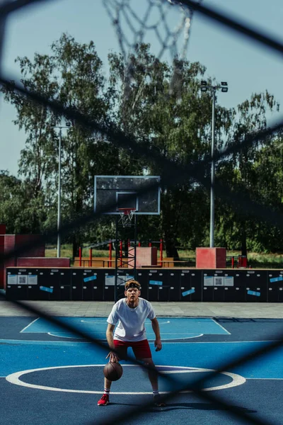full length of basketball player training on modern court on blurred foreground