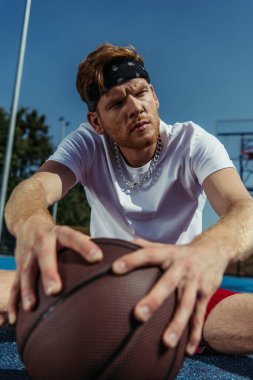 sportive man in necklace and bandana looking away near blurred ball