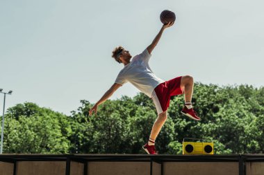 side view of man in sportswear playing basketball near record player