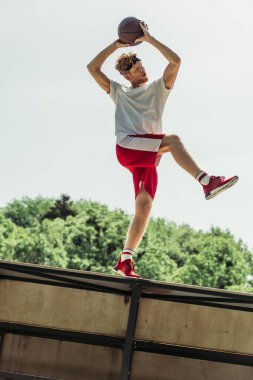 low angle view of sportive man playing basketball outdoors in summer