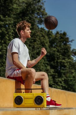 redhead man playing with ball while sitting near boombox