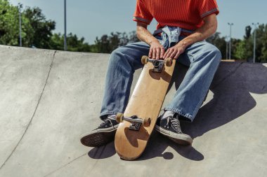 cropped view of skater in jeans sitting on ramp in skate park