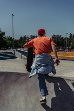 back view of man in orange t-shirt running on ramp with skateboard