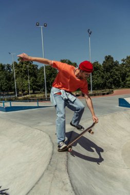 young fashionable man training on skateboard on ramp in park