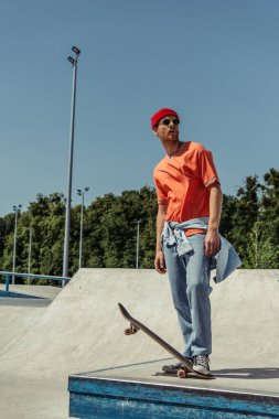 full length of man in orange t-shirt and sunglasses standing in skate park