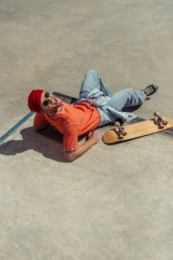 high angle view of laughing skater lying near skateboard on ramp